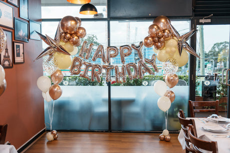 Happy Birthday foil lettering framed by a balloon garland in a private room