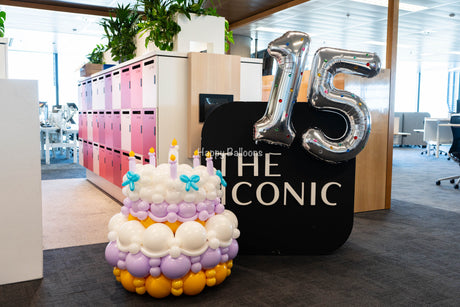 Completed white, lilac and orange balloon cake with silver number 15 at a Sydney office event
